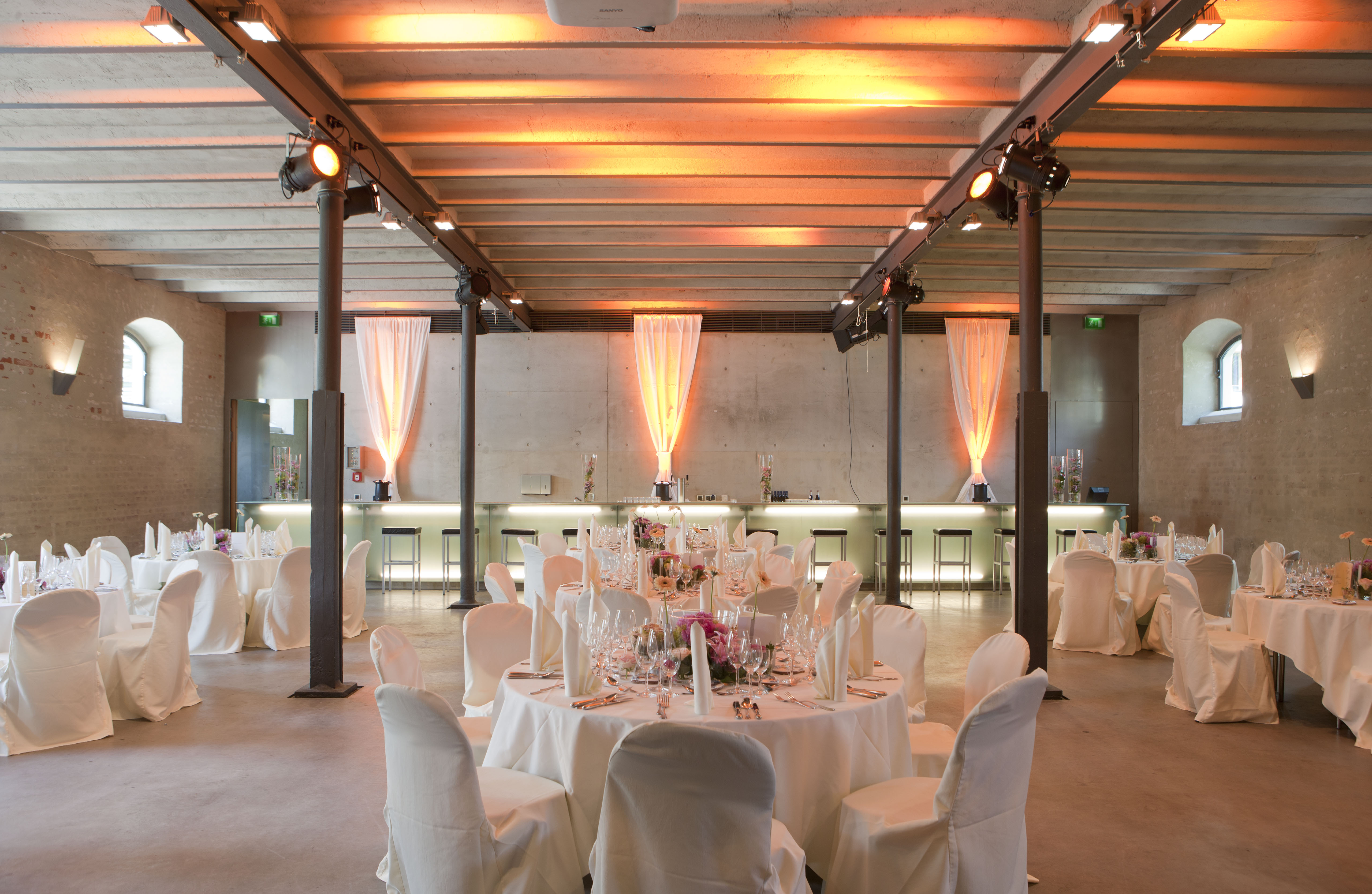 Hochzeitslocation - Schlicht und elegant ist der ebenerdige Säulensaal mit seinen gusseisernen Stützsäulen, den geschlämmten Ziegelwänden und der dezent beleuchteten Glastheke an der hinteren Wand.  - Fürstenfelder Gastronomie & Hotel GmbH