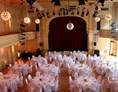 Hochzeitslocation: Festlicher Ballsaal mit runden Tischen und Bankett-Bestuhlung mit weißen Stuhl-Hussen - Heimathafen Neukölln