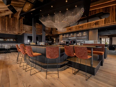 Hochzeitslocation: Unser Stolz: unsere kommunikative und große Bar, eingebettet in die Kombination von traditionellem Hüttenambiente mit viel Altholz und modernem Style. Sie lädt ein zum Verweilen mit Freunden, zum gemeinsamen Drink während der Partynacht oder einfach zum Genießen der wunderschönen Aussicht. Highlight ist unser Kristall-Adler, welcher für ein besonderes Ambiente sorgt und abends unser Restaurant in ein besonderes Licht verzaubert. - jezz AlmResort Ellmau
