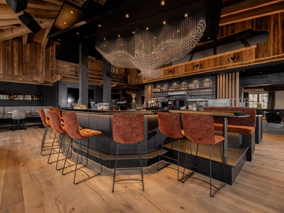 Winterhochzeit - Bezirk Kufstein - Unser Stolz: unsere kommunikative und große Bar, eingebettet in die Kombination von traditionellem Hüttenambiente mit viel Altholz und modernem Style. Sie lädt ein zum Verweilen mit Freunden, zum gemeinsamen Drink während der Partynacht oder einfach zum Genießen der wunderschönen Aussicht. Highlight ist unser Kristall-Adler, welcher für ein besonderes Ambiente sorgt und abends unser Restaurant in ein besonderes Licht verzaubert. - jezz AlmResort Ellmau