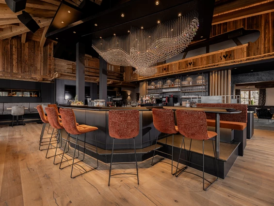Hochzeitslocation: Unser Stolz: unsere kommunikative und große Bar, eingebettet in die Kombination von traditionellem Hüttenambiente mit viel Altholz und modernem Style. Sie lädt ein zum Verweilen mit Freunden, zum gemeinsamen Drink während der Partynacht oder einfach zum Genießen der wunderschönen Aussicht. Highlight ist unser Kristall-Adler, welcher für ein besonderes Ambiente sorgt und abends unser Restaurant in ein besonderes Licht verzaubert. - jezz AlmResort Ellmau