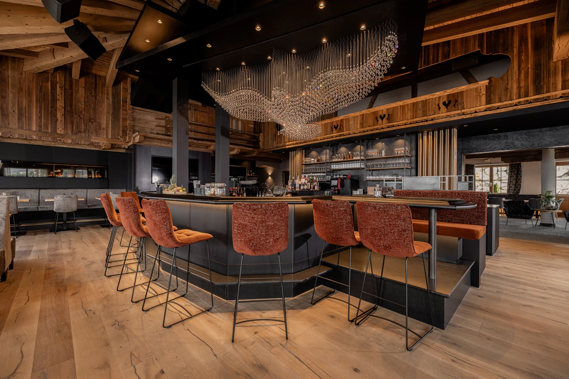 Hochzeitslocation: Unser Stolz: unsere kommunikative und große Bar, eingebettet in die Kombination von traditionellem Hüttenambiente mit viel Altholz und modernem Style. Sie lädt ein zum Verweilen mit Freunden, zum gemeinsamen Drink während der Partynacht oder einfach zum Genießen der wunderschönen Aussicht. Highlight ist unser Kristall-Adler, welcher für ein besonderes Ambiente sorgt und abends unser Restaurant in ein besonderes Licht verzaubert. - jezz AlmResort Ellmau